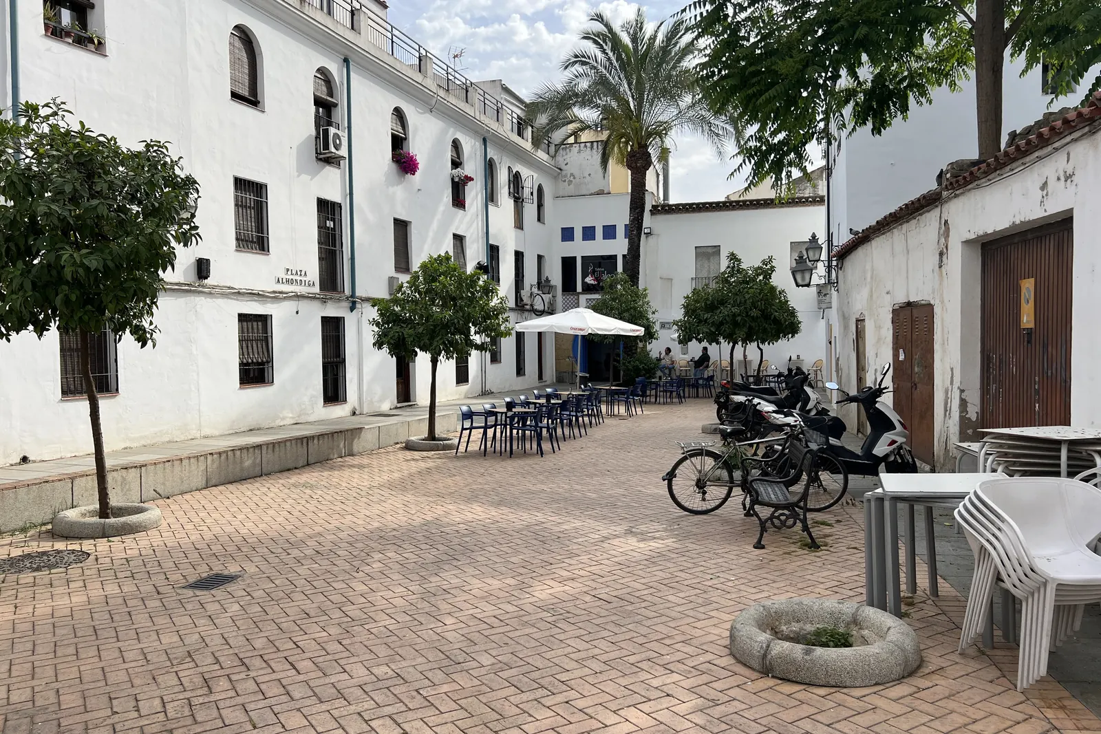 Plaza Alhóndiga in Córdoba, a paved square with orange trees, café tables and whitewashed buildings under a bright sky