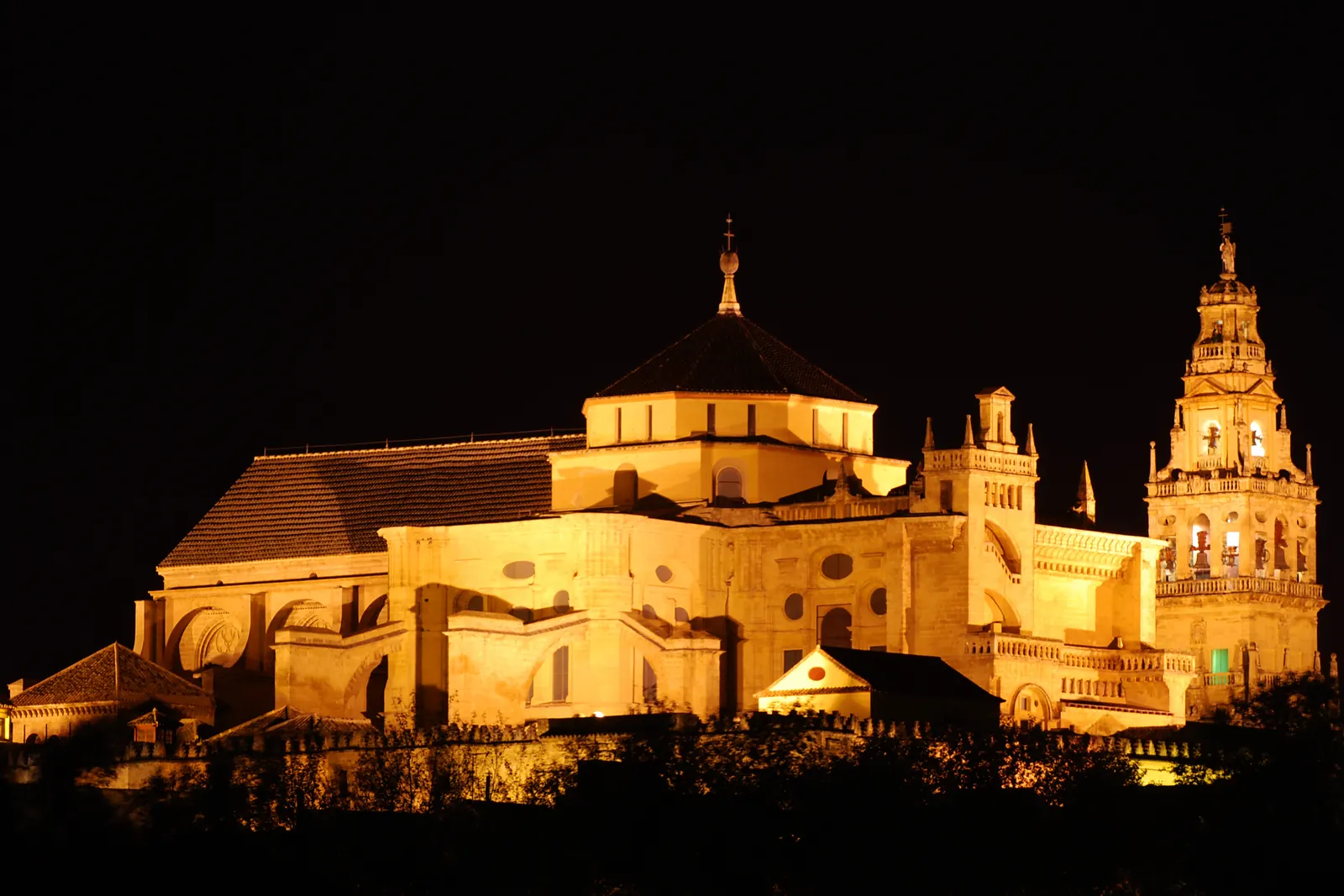 The Mosque-Cathedral of Córdoba floodlit in gold against the night sky, with its bell tower on the right